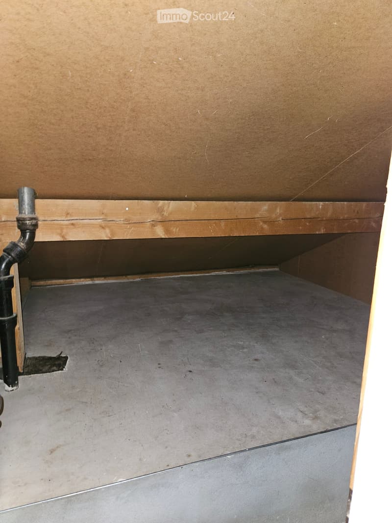 Empty room with a concrete floor and exposed wooden framing, showing a small gap between the floor and the wall.