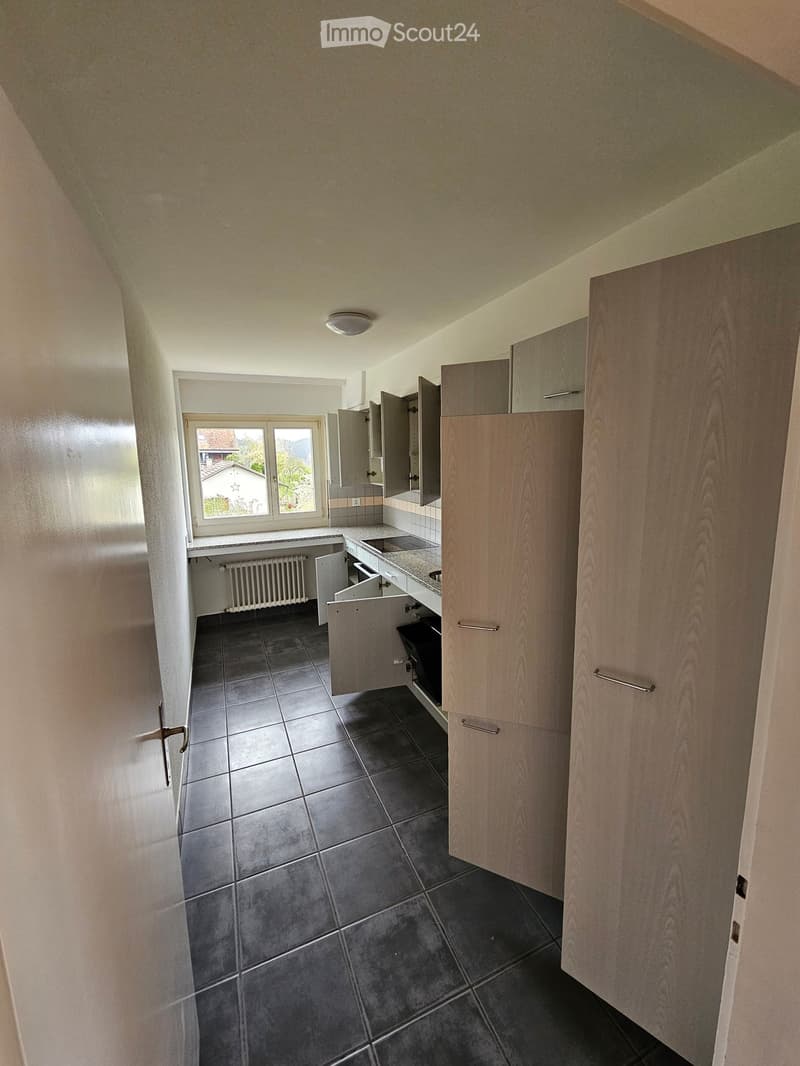 Empty kitchen with dark tiled floor, light wooden cabinets, and a window overlooking a residential area.
