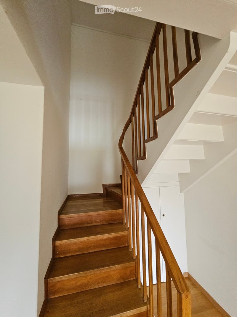 Wooden staircase with a wooden handrail and white walls.