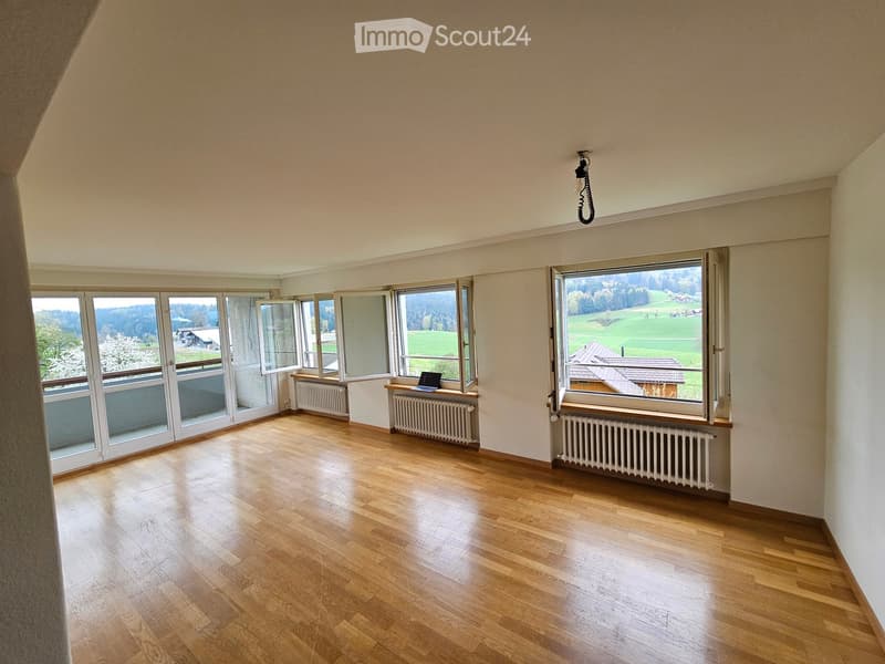 Empty room with wooden flooring, large windows, radiators, and a hanging light fixture.