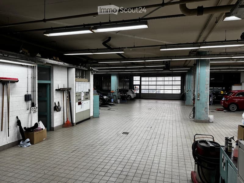 Garage with tiled floor, white brick walls, fluorescent lighting, and several parked cars. Cleaning tools and supplies are visible along the walls.
