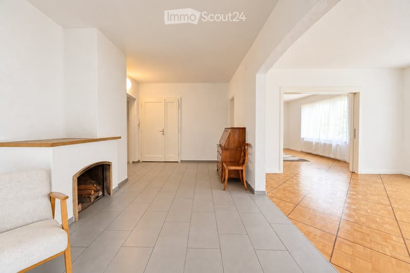 Bright living room with a fireplace, a sofa, a wooden chair, and a cabinet, featuring tiled and wooden flooring.