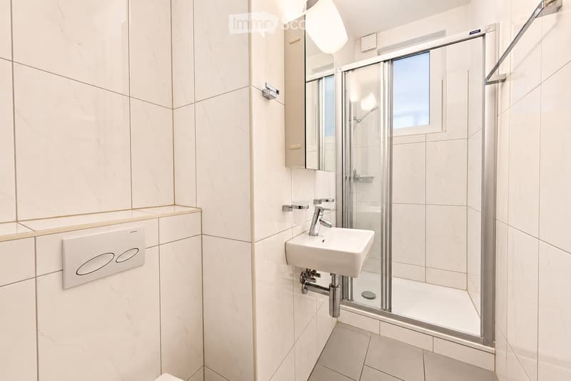 Modern bathroom with white marble tiles, a white sink, a glass-enclosed shower, and a mirrored cabinet with a built-in light fixture.