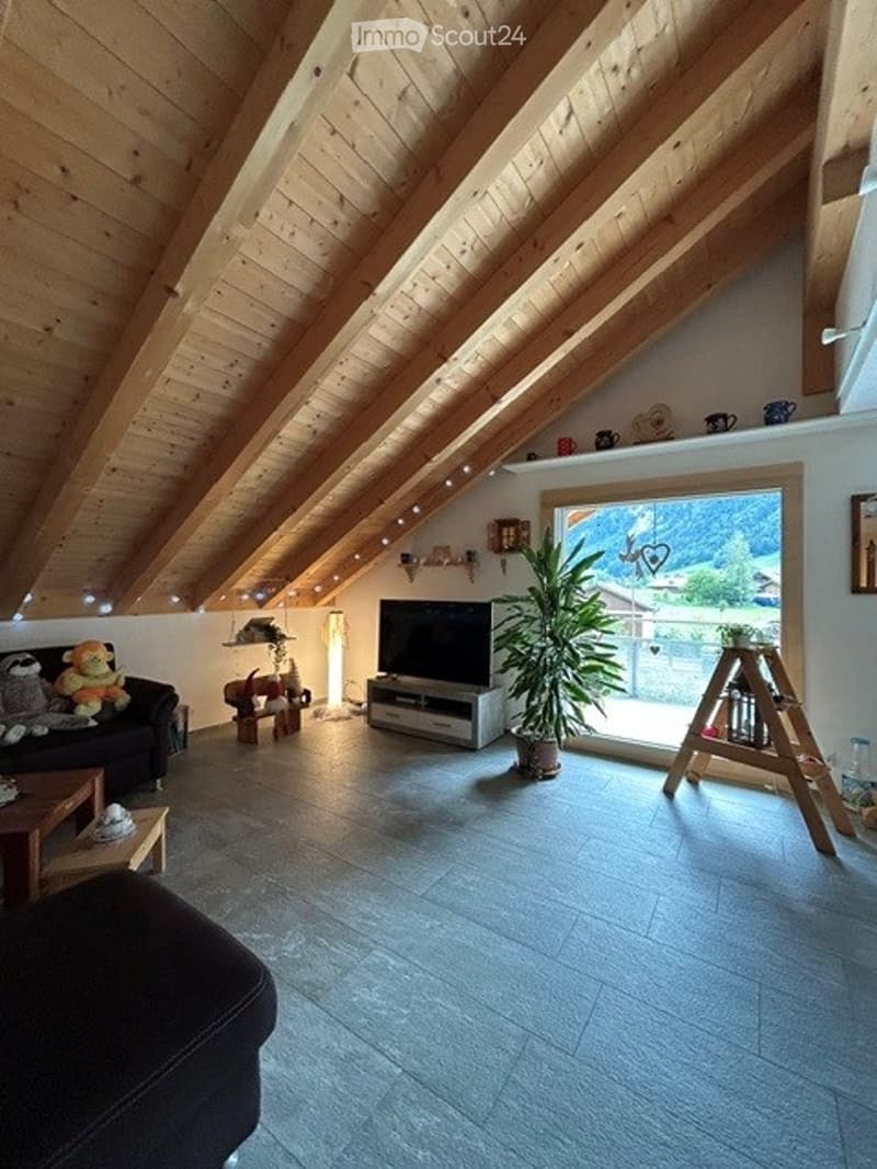 Bright living room with exposed wooden beams, large window offering a scenic view, modern furniture including a sofa, coffee table, TV, and decorative plant.