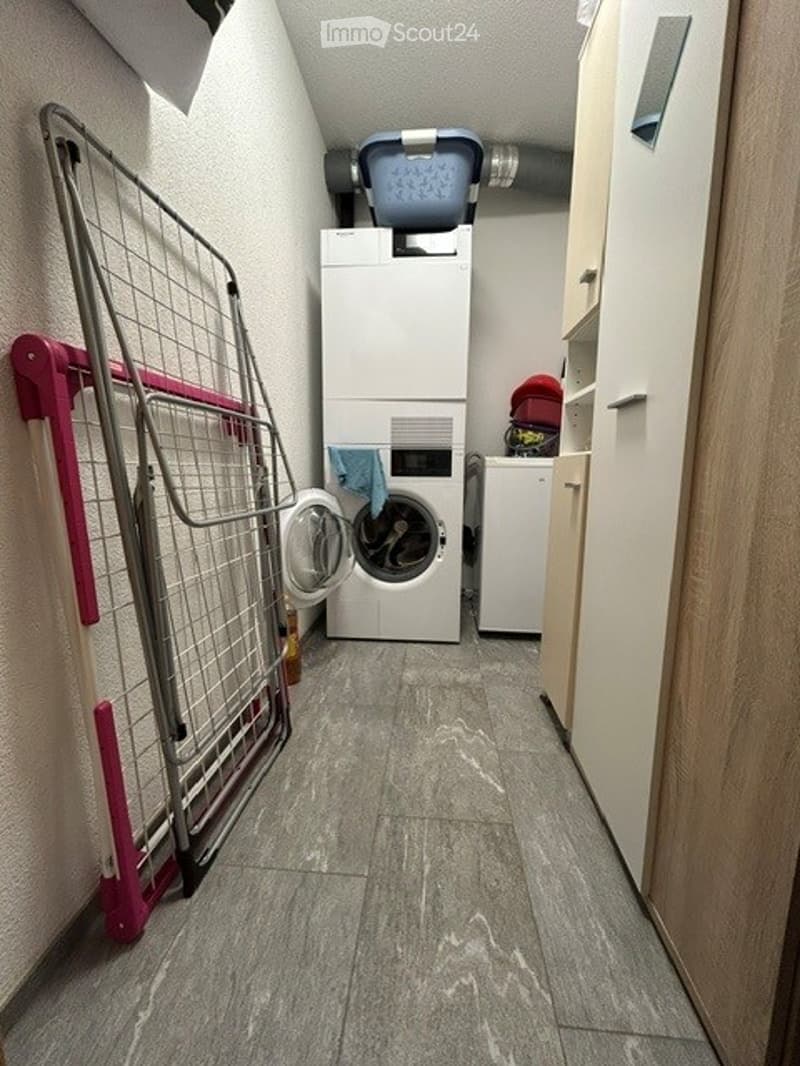 A narrow laundry area with a washing machine, dryer, a laundry basket on top, a towel hanging on the dryer, and a cabinet on the right side.