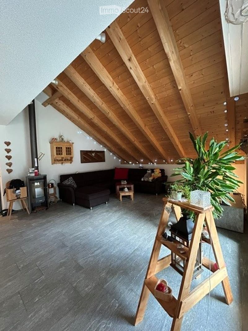 Living room with exposed wooden beams, grey sofa, coffee table, small plant, and decorative items on a shelf.