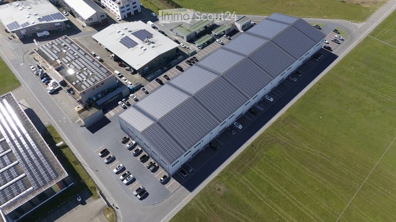 An industrial building with multiple structures, large parking lot, and solar panels on the roofs