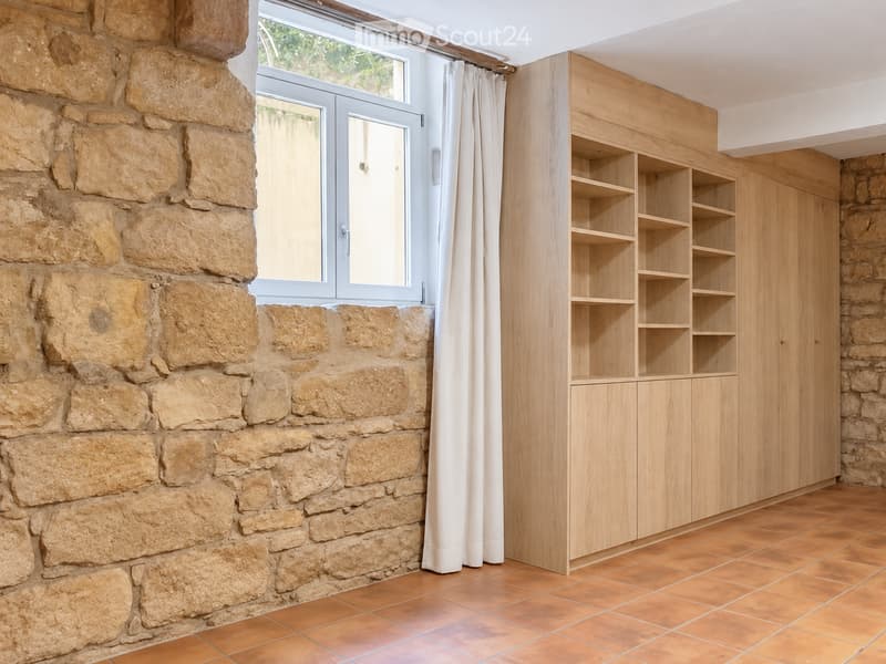 Empty room with stone walls, wooden shelving unit, and large window with white curtains.