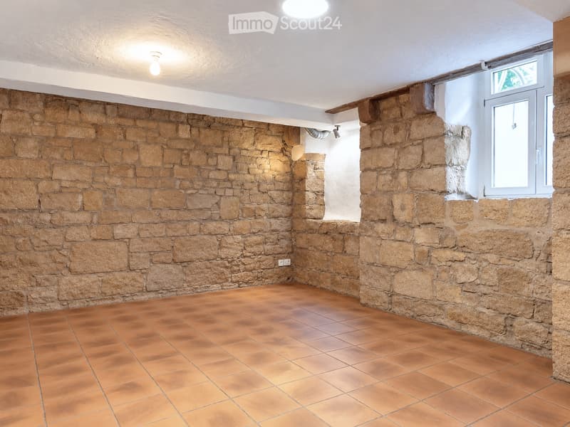 Empty room with stone walls and terracotta tiled floor, featuring a small window and recessed lighting.