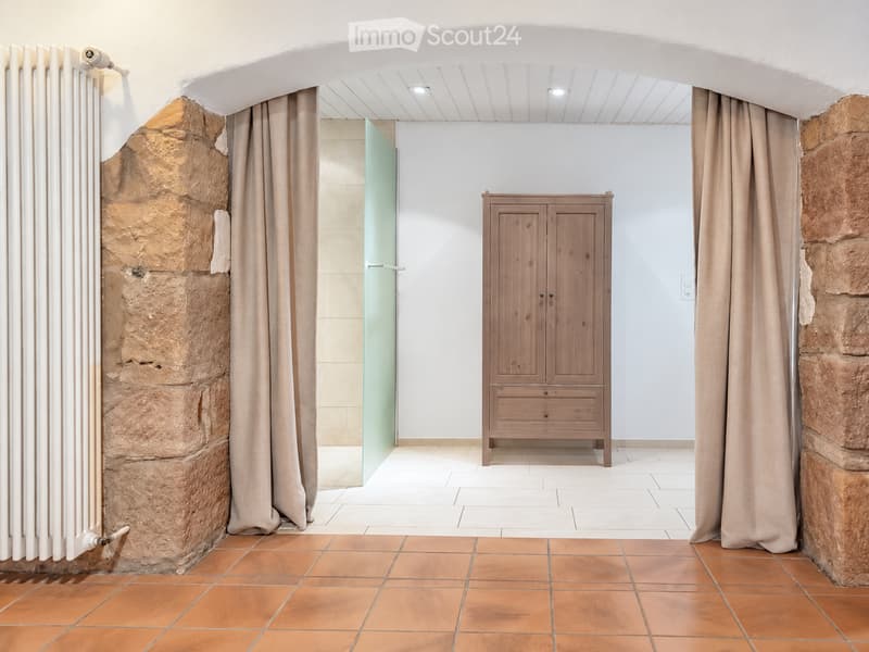 A room with exposed stone walls, a wooden cabinet, and a glass shower enclosure partially visible behind a curtain.