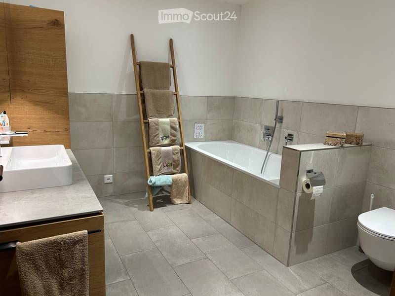 Modern bathroom with a white sink, bathtub, toilet, and a wooden towel ladder holding multiple towels.