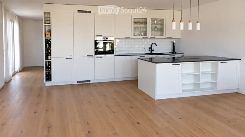 Modern kitchen with white cabinets, a central island, pendant lights, and a wine rack. The floor is made of light wooden planks.