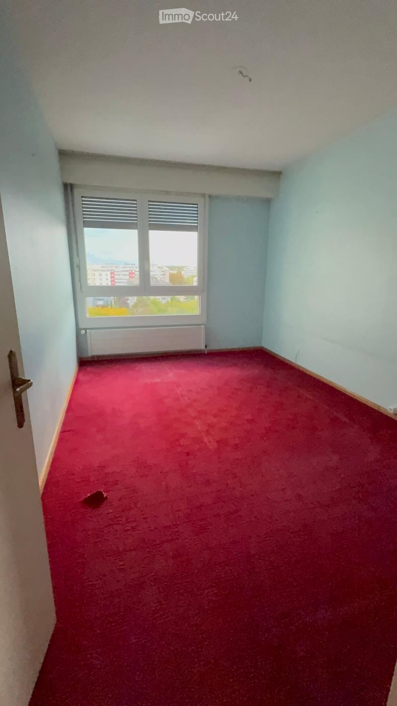 Empty room with red carpet, light blue walls, and a window with blinds. No furniture or equipment present.