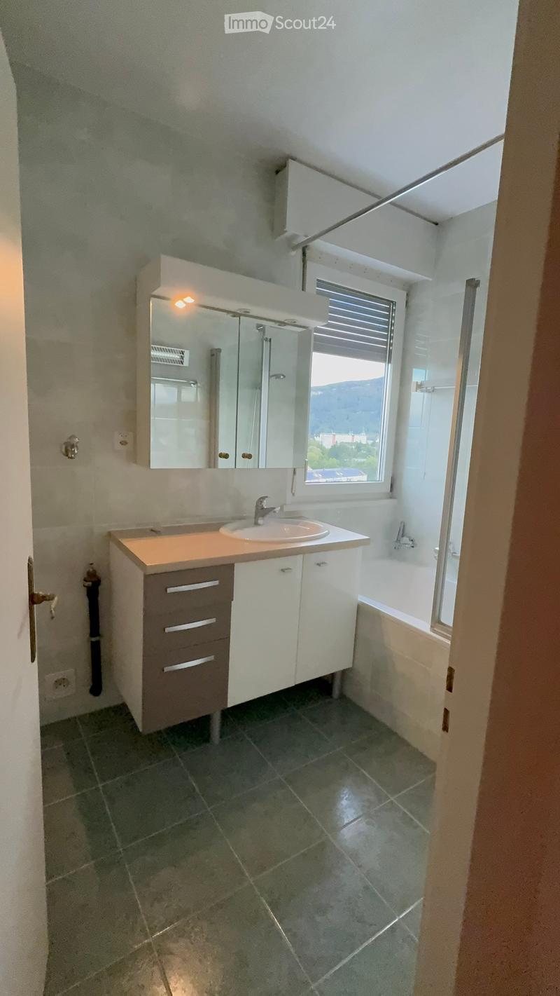 Modern bathroom with a white sink, mirror, and cabinet, featuring a window with blinds and tiled flooring.