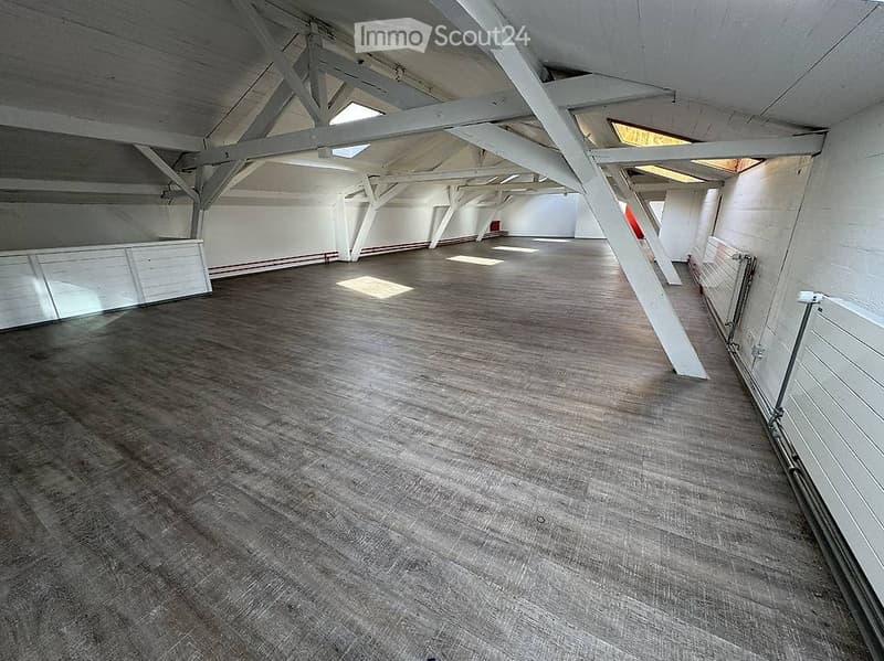 Empty room with wooden floor, white walls, exposed wooden beams, and natural light from skylights.
