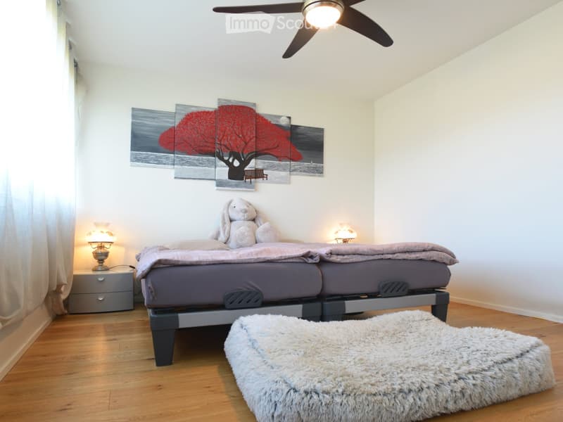 Cozy bedroom with a double bed, nightstands, lamps, a fluffy rug, and a decorative wall art featuring a tree and a bench.