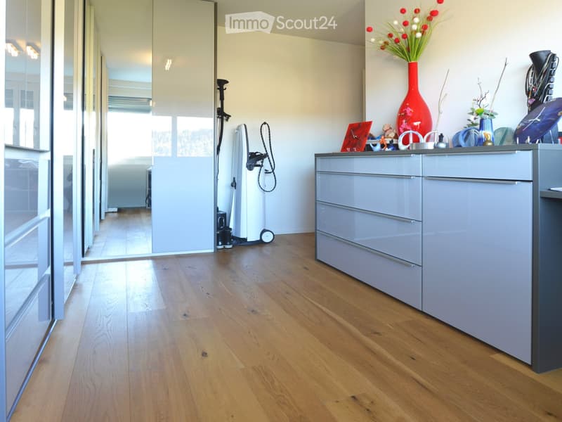 Modern hallway with light wooden flooring, grey cabinet, decorative vase, and artwork on the wall.