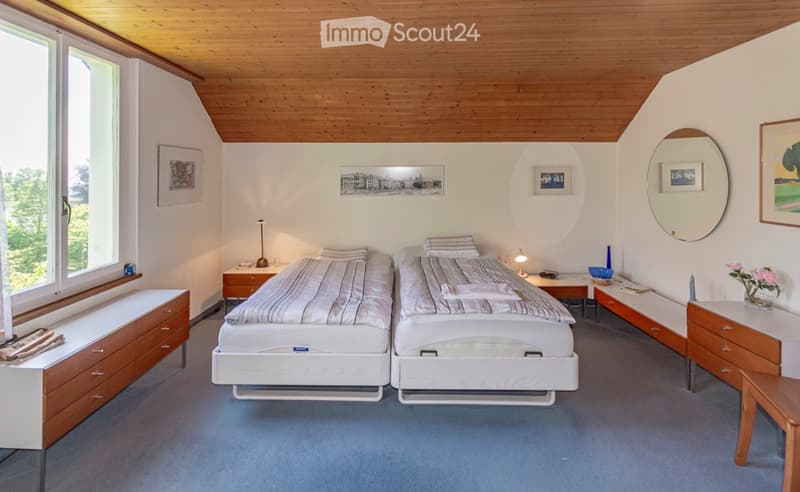 Bright bedroom with two single beds, nightstands, a large mirror, and decorative items including a vase with flowers and picture frames on the walls.