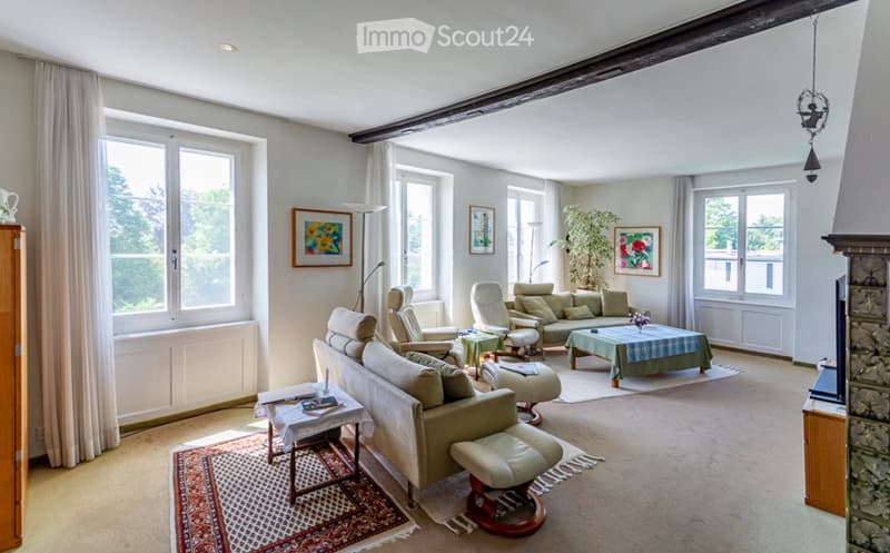 Bright living room with large windows, cream-colored sofa, armchairs, coffee tables, floor lamp, and artwork on the walls.