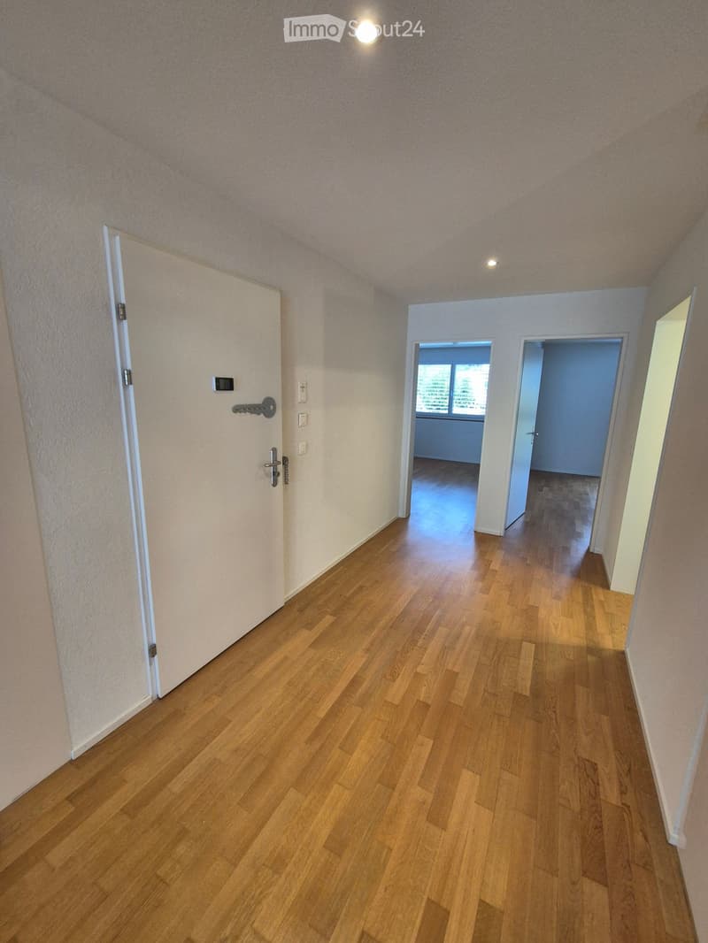 Empty hallway with wooden flooring, white walls, and several doors leading to other rooms.