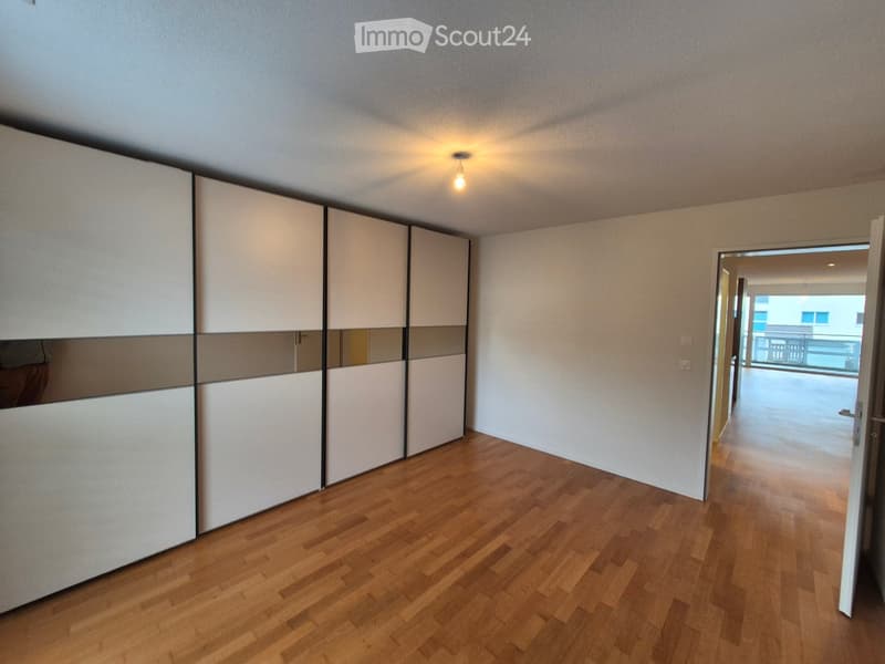 Empty room with wooden flooring, white walls, and a large sliding wardrobe unit. An open doorway leads to a balcony area.