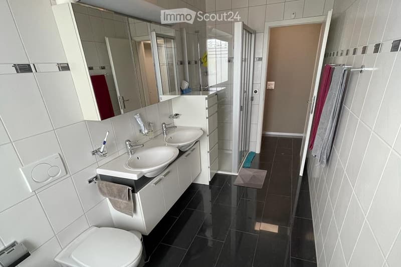 Modern bathroom with double sink, large mirror, toilet, and tiled walls and floor. Towels are neatly placed on the cabinet and a rack.