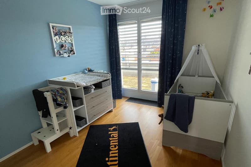 Brightly lit children's bedroom with a changing table, crib, storage unit, and a rug on the floor.