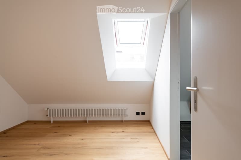 Empty room with wooden flooring, white walls, a radiator, and a skylight window above the door.