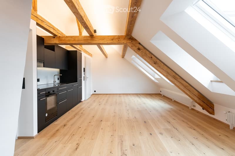 Bright, open kitchen with wooden beams, light wooden flooring, and modern black kitchen cabinets.