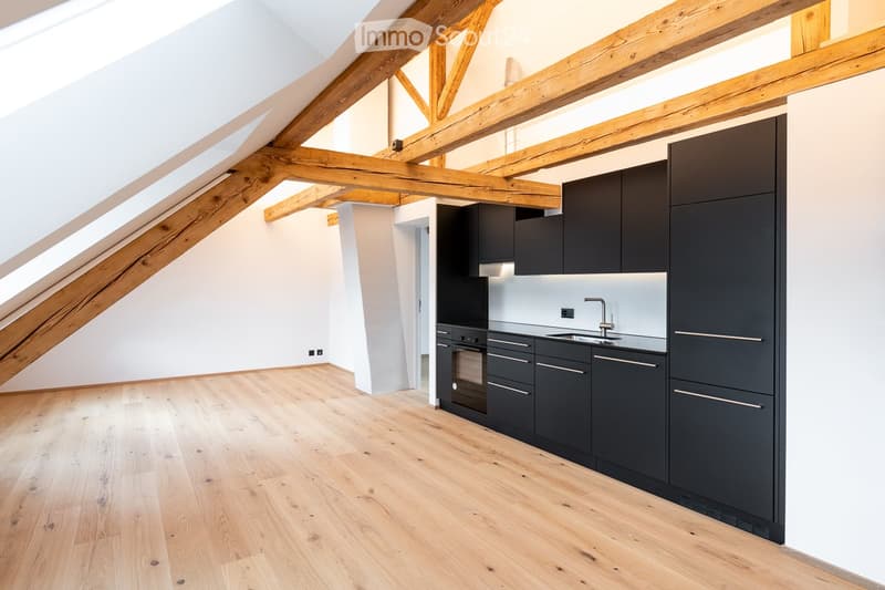 Modern kitchen with dark grey cabinets, a stainless steel sink, and a wooden floor. The ceiling features exposed wooden beams and skylights.