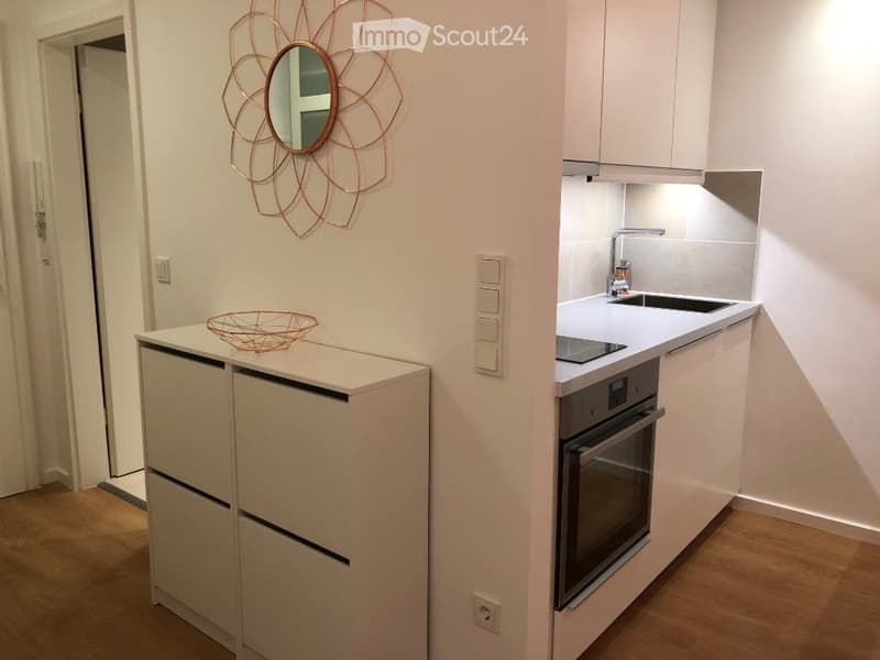 Modern kitchen with white cabinets, a sink, a faucet, an oven, a decorative mirror, and a bowl on the counter.
