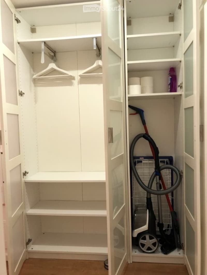 A well-organized closet with white cabinetry, shelves, and a vacuum cleaner stored inside. The closet features built-in storage with multiple shelves and hanging space.