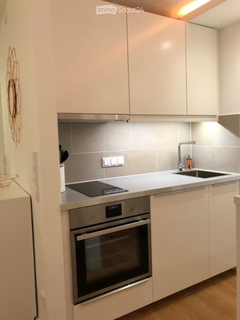 Modern kitchen with white cabinets, stainless steel appliances, and a sleek design. Features an induction cooktop, oven, and a sink with a modern faucet.