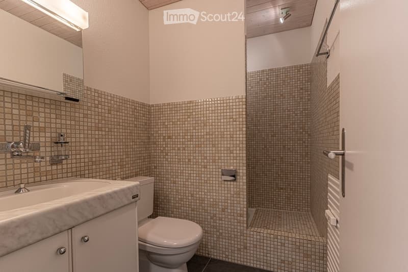 Modern bathroom with beige tiled walls, a marble sink, a toilet, and a shower area with a glass door. The space features a sleek design with built-in storage and a modern faucet.