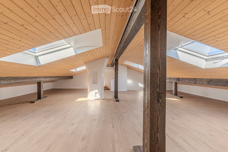 Bright, open loft space with wooden floors, exposed wooden beams, and skylights allowing natural light to flood the room. The space is completely unfurnished, showcasing the architectural details and clean lines of the design.