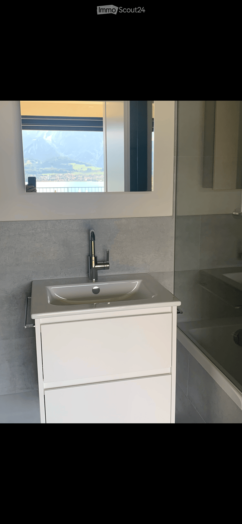 modern design with gray wall tiles, white vanity with 3 drawers, modern faucet, view from the mirror to outside with a lake and mountain