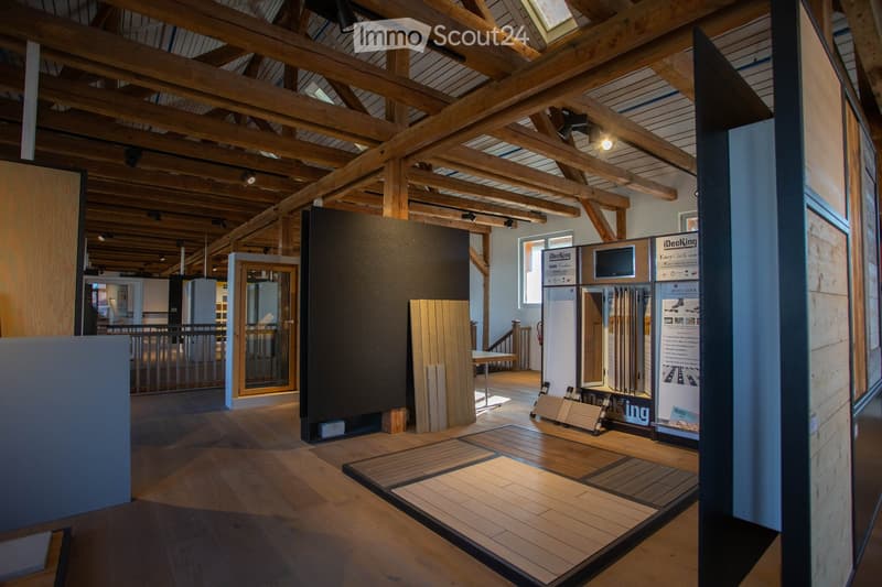 A spacious showroom with exposed wooden beams and a high ceiling, featuring various wooden decking samples and display boards.