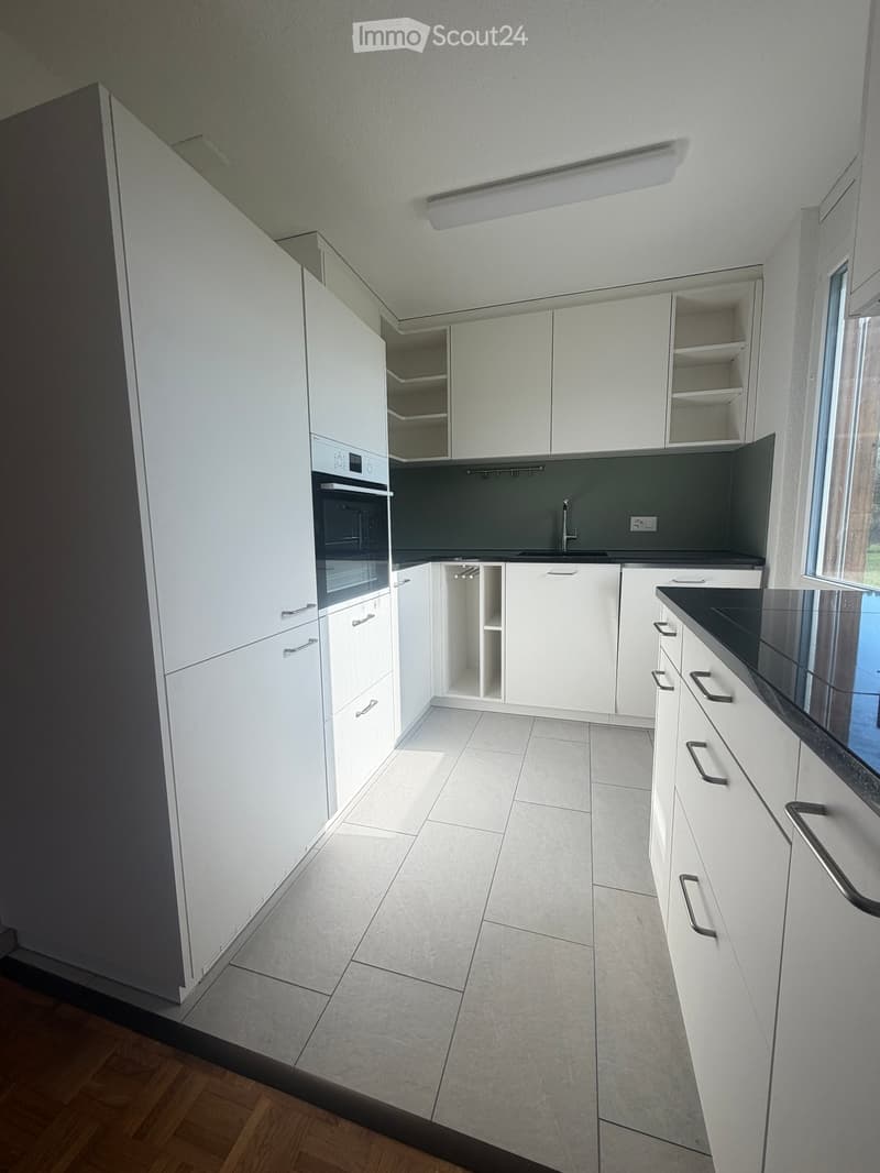 Modern kitchen with white cabinets, a black countertop, and a built-in oven. The space features tiled flooring and a window providing natural light.