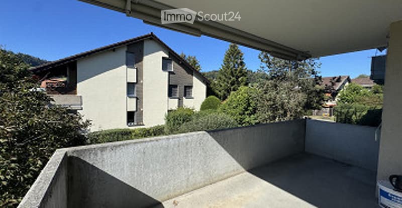 Empty concrete balcony with a view of a residential building and surrounding greenery.