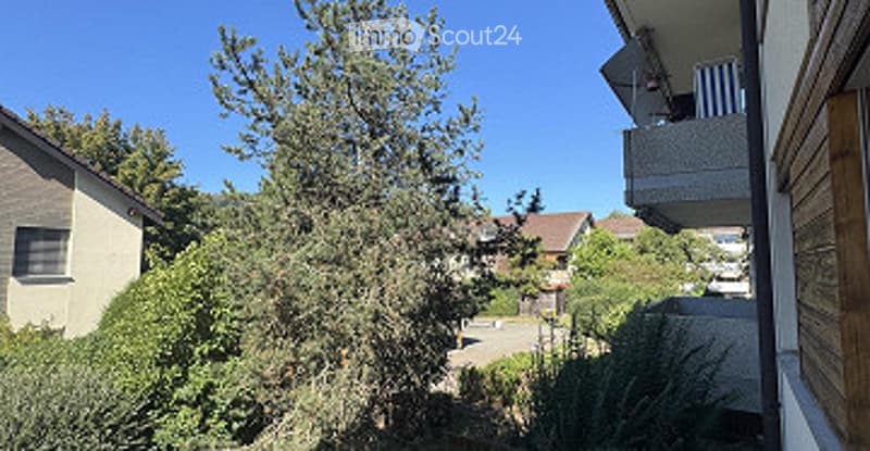 Balcony overlooking a residential area with trees, neighboring houses, and a clear blue sky.
