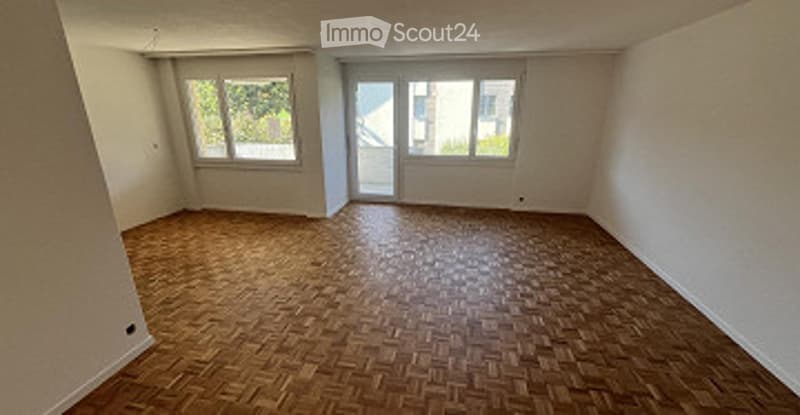 Completely empty room with wooden parquet flooring, white walls, and large windows with blinds. No furniture or equipment.