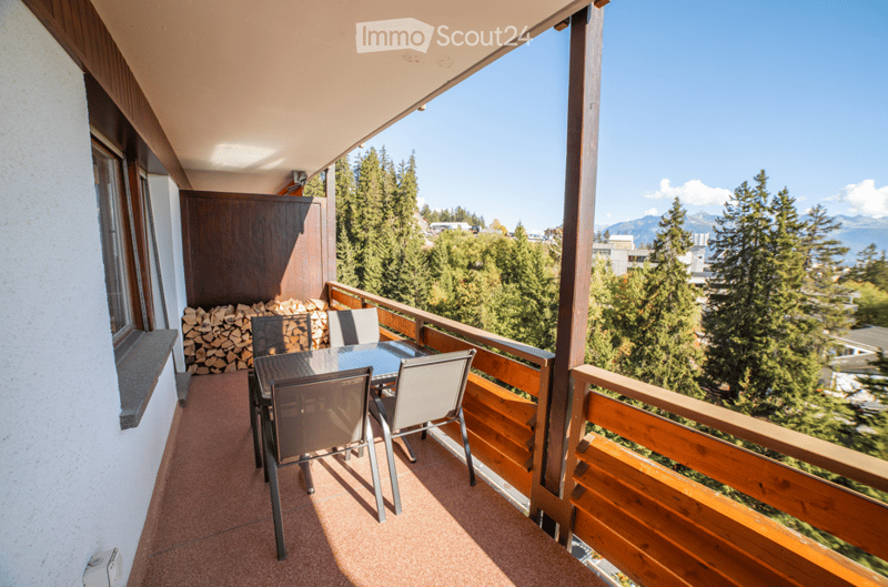 Balcony with wooden railing, table, chairs, and scenic mountain view.