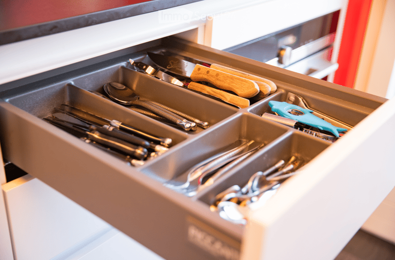 Open kitchen drawer with neatly organized utensils including knives, spoons, tongs, and scissors in labeled compartments.