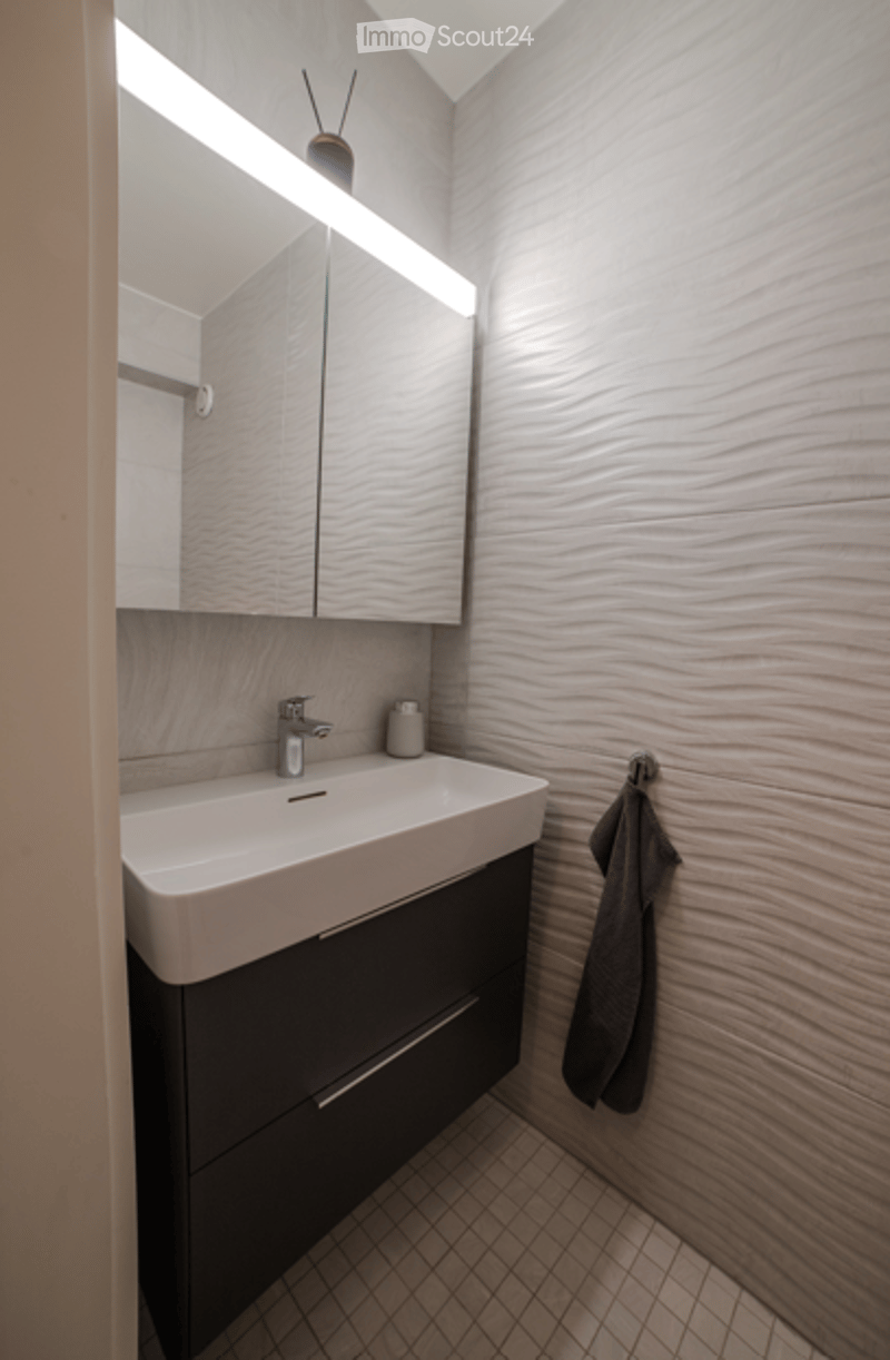 Modern bathroom with a sleek sink, mirrored cabinet, and a towel hanging on a rack.