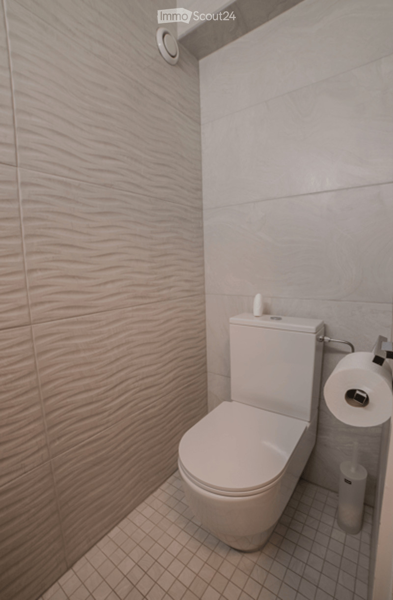 Modern bathroom with a sleek white toilet, textured light wood wall tiles, and a small toilet paper holder with a roll of toilet paper.