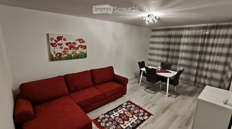 A modern, open-concept living and dining area with a red sectional sofa, a white dining table with black chairs, a patterned rug, and a painting on the wall.