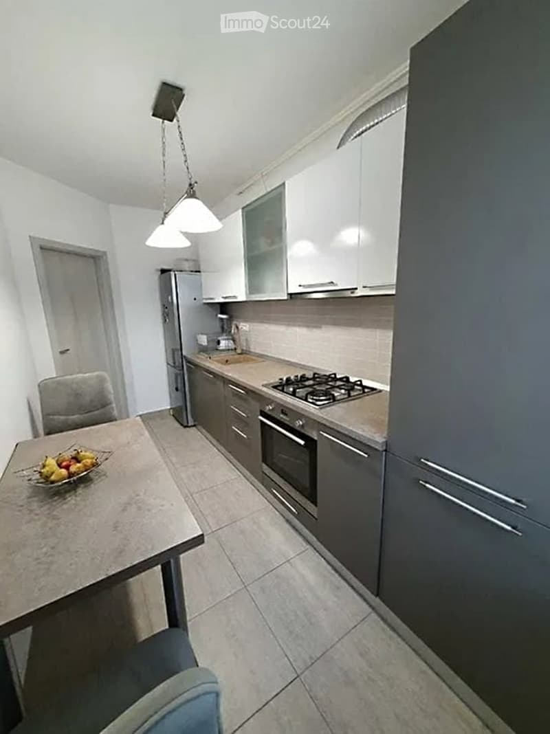 Modern kitchen with white and grey cabinets, stainless steel appliances, gas stove, refrigerator, and a small dining area with a table and chairs.