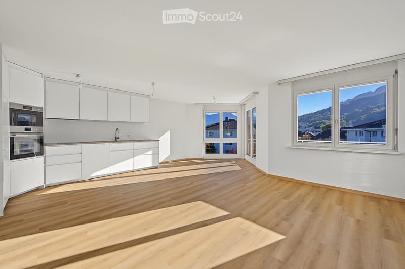Modern, minimalist kitchen with white cabinets, stainless steel oven, and large windows offering a scenic mountain view.