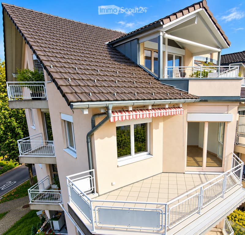 Two-story house with brown tiled roof, multiple balconies, and striped awnings over windows.