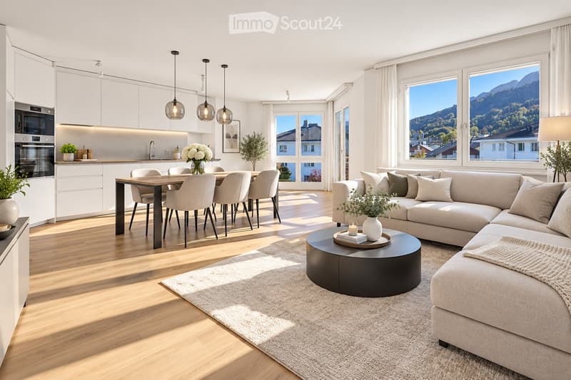 Modern open-plan living and dining area with large windows offering a scenic mountain view. Features a light grey sectional sofa, round coffee table, dining table with six chairs, white kitchen cabinets, and pendant lights.